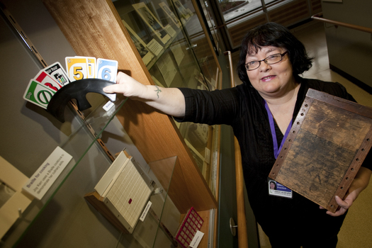 Michele Prentice holding a card holder with Braille UNO cards and a base board for a braille frame