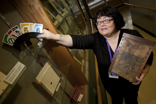 Michele Prentice holding a card holder with Braille UNO cards and a base board for a braille frame
