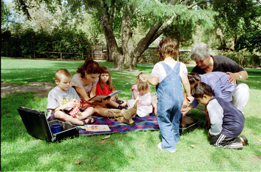 Sigrid and various children sit on or stand beside a picnic blanket