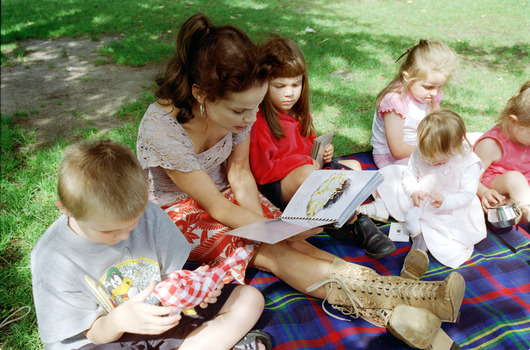 Sigrid and various children sit on a picnic blanket in a grassed area