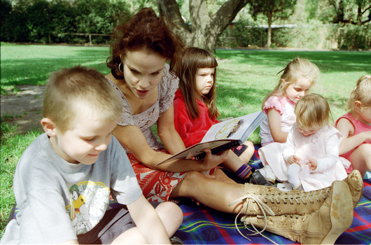 Sigrid and various children sit on a picnic blanket in a grassed area