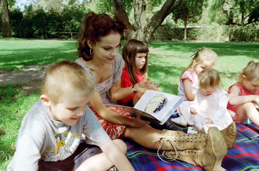 Sigrid and various children sit on a picnic blanket in a grassed area