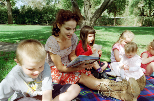 Sigrid and various children sit on a picnic blanket in a grassed area