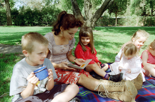 Sigrid and various children sit on a picnic blanket in a grassed area