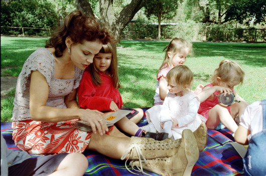 Sigrid and various children sit on a picnic blanket in a grassed area