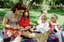 Sigrid and various children sit on a picnic blanket in a grassed area