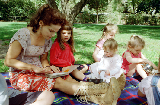 Sigrid and various children sit on a picnic blanket in a grassed area