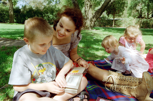 Sigrid and various children sit on a picnic blanket in a grassed area