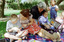 Sigrid and various children sit on a picnic blanket in a grassed area