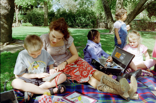 Sigrid and various children sit on a picnic blanket in a grassed area