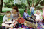 Sigrid and various children sit on a picnic blanket in a grassed area