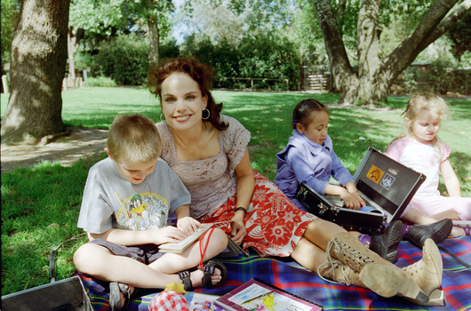 Sigrid and various children sit on a picnic blanket in a grassed area