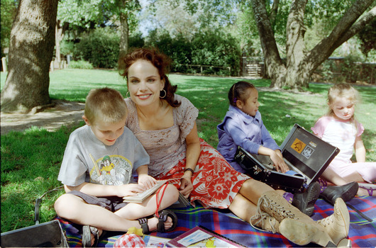Sigrid and various children sit on a picnic blanket in a grassed area