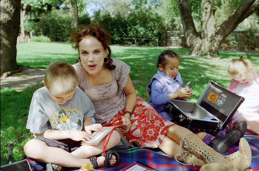 Sigrid and various children sit on a picnic blanket in a grassed area