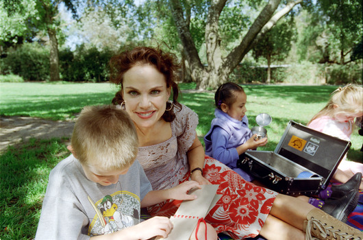 Sigrid and various children sit on a picnic blanket in a grassed area