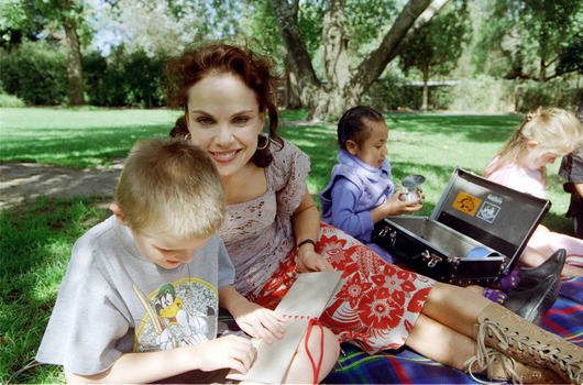 Sigrid and various children sit on a picnic blanket in a grassed area