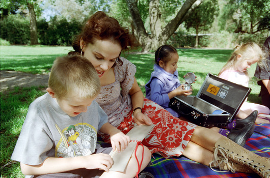 Sigrid and various children sit on a picnic blanket in a grassed area