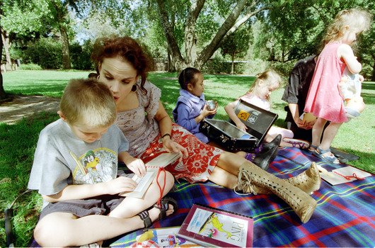 Sigrid and various children sit on a picnic blanket in a grassed area