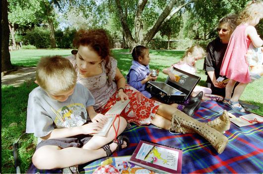 Sigrid and various children sit on a picnic blanket in a grassed area