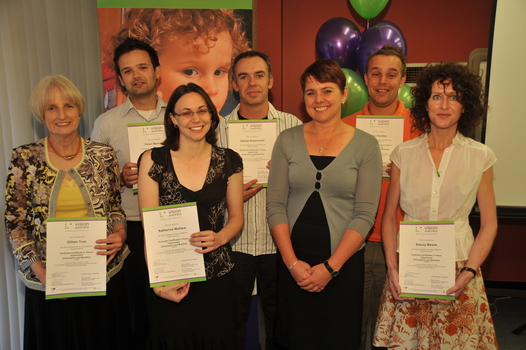 Six people stand holding their certificates with another person