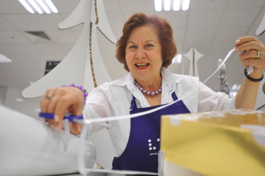 Woman in white shirt and purple apron cutting ribbon on gift wrap table