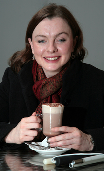 Renee sitting in the Kooyong cafe with a hot chocolate and white cane on the table