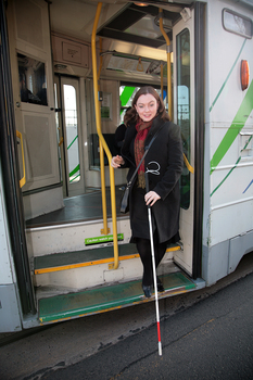 Renee disembarking from a tram with her white cane