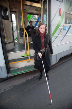 Renee disembarking from a tram with her white cane