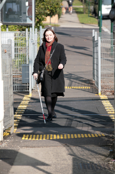 Renee crossing the train tracks at Kooyong station using her white cane