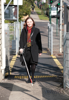 Renee crossing the train tracks at Kooyong station using her white cane