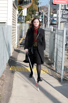 Renee crossing the train tracks at Kooyong station using her white cane