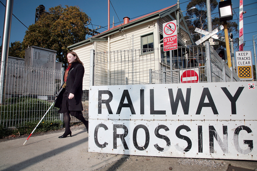 Renee crossing the train tracks at Kooyong station using her white cane