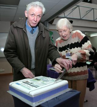 Norm Rees and Pam Adams start to cut the cake made for the 25th Anniversary of Vision Australia Radio