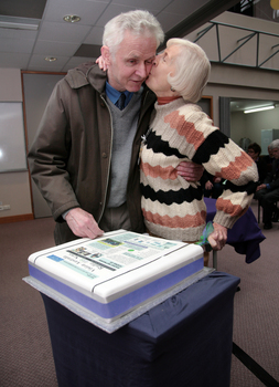 Norm Rees receives a kiss from Pam Adams as she slices into the cake made for the 25th Anniversary of Vision Australia Radio