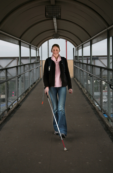 Anna using an overpass at a train station with her cane