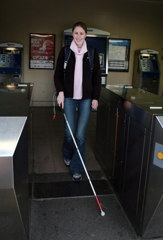 Anna going through the ticket gate at a train station with her cane