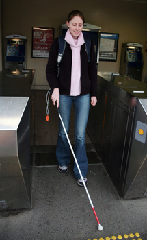 Anna going through the ticket gate at a train station with her cane