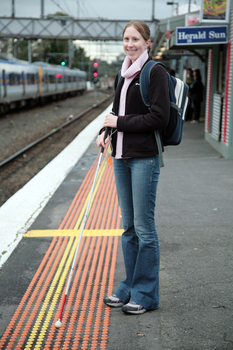Anna waiting on the platform at a train station with her cane