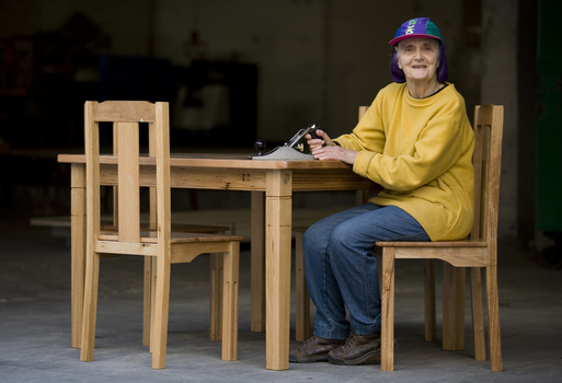 Elderly lady sits a wooden table with a planer in her hands