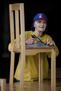 Elderly woman stands by a raised chair with planer in her hands