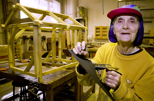 Elderly woman stands in a workshop with planer in her hands
