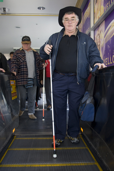 Male prepares to descend the escalator with his cane