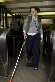 Female white cane user navigates the ticketed entry