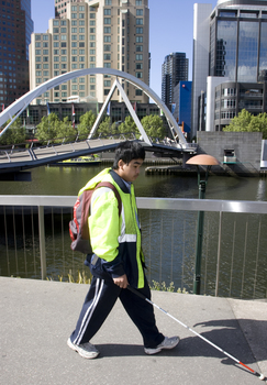White cane user walking along river path at Southbank on a sunny day