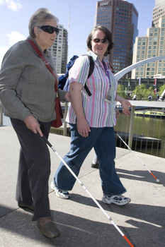 White cane user walking along river path at Southbank on a sunny day