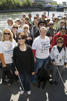 Group of people holding white canes or holding dogs pose beside Yarra River and Princess Bridge