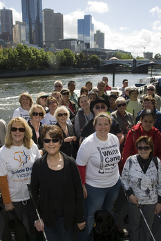 Group of people holding white canes or holding dogs pose beside Yarra River and Princess Bridge