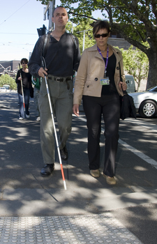 White cane users walking along the St Kilda Road footpath on a sunny day