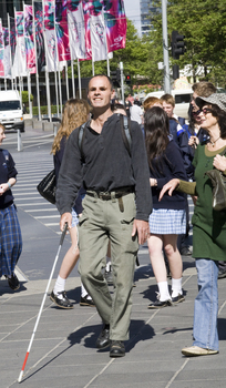 White cane user walking along the St Kilda Road footpath on a sunny day