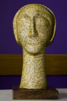 Sculpture of head on long neck made from yellow paper with copperplate writing